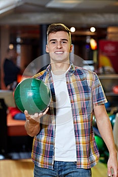 Happy young man holding ball in bowling club