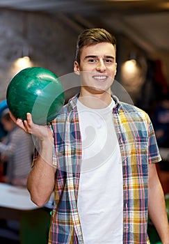 Happy young man holding ball in bowling club