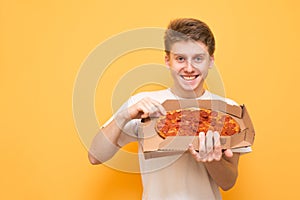 Happy young man holding a box of fresh pizza from the delivery, looking into the camera and smiling, isolated. Portrait of a