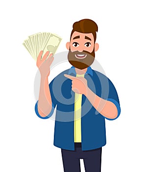 Happy young man holding cash/money/banknotes and pointing his index finger towards that. Financial money concept. Human emotion.