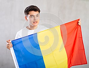 Happy young man holding flag of Romania against unicoloured background