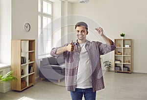 Happy young man holding keys to his new house or apartment and showing thumbs up