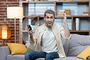 Happy young man holding phone in hand, happy and celebrating, looking and shouting at camera. Got good news, messages