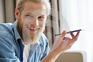Happy young man holding phone using virtual voice assistant looking at camera.