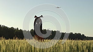 Happy young man joyfully greets an airplane flying in the sky in a wheat field in the summer at sunset. Dream, travel