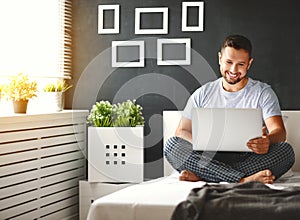 Happy young man with laptop in bed