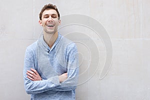 Happy young man laughing by wall with arms crossed