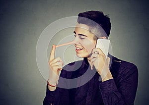 Happy young man liar with long nose talking on mobile phone