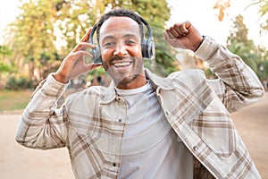 Happy young man listening music and dancing with headphones on the street. Space for text