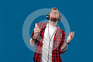 Happy young man listening to music with headphones. Handsome smiling guy in checkered shirt with closed eyes dancing