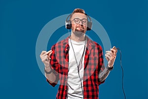 Happy young man listening to music with headphones. Handsome smiling guy in checkered shirt with closed eyes dancing