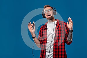 Happy young man listening to music with headphones. Handsome smiling guy in checkered shirt dancing and singing with