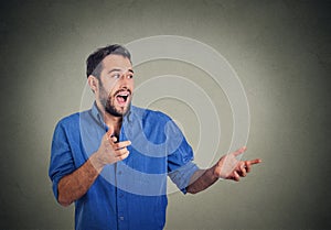 Happy young man looking to side while pointing at you, surprised by something