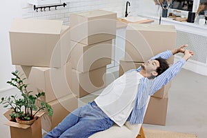 happy young man, lying in armchair resting after packing boxes with personal belongings