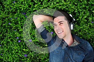 Happy young man lying on grass, listening to music