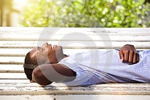Happy young man lying on park bench with headphones