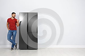 Happy young man near refrigerator indoors, space for text