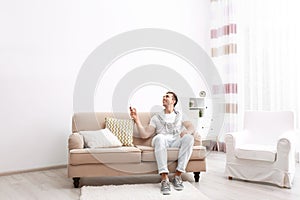 Happy young man operating air conditioner with remote control