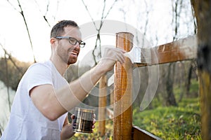 Happy young man painting wooden fence on beautiful spring afternoon