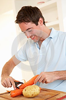 Happy young man peeling vegetable in kitchen