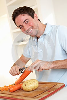 Happy young man peeling vegetable in kitchen