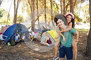 Happy young man piggybacking woman with friends in background