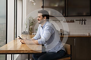 Happy young man pondering on phone message from beloved woman