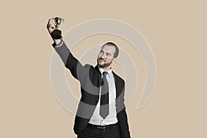 Happy young man raising winning trophy over colored background