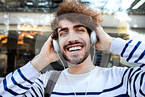 Happy young man relaxing outdoors listening to music using headphones looking at camera.