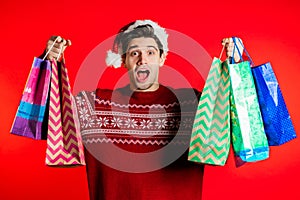 Happy young man in Santa hat.colorful paper bags after shopping isolated on red