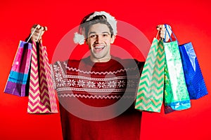 Happy young man in Santa hat.colorful paper bags after shopping isolated on red