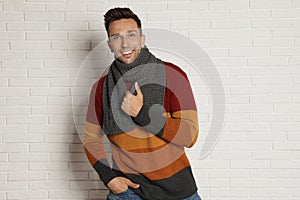 Happy young man in scarf and warm sweater near wall. Winter season