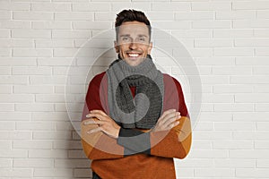 Happy young man in scarf and warm sweater near white brick wall