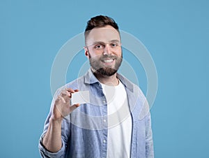 Happy young man showing empty business card with space for design over blue studio background