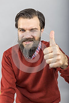 Happy young man showing OK sign with his thumb up and blinking