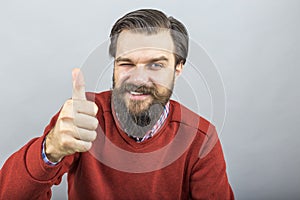 Happy young man showing OK sign with his thumb up and blinking