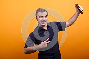 Happy young man showing victory sign and holding mobile phone over yellow backdround