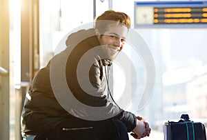 Happy young man sitting with bag at train station