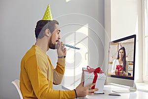 Happy young man sitting at computer and having virtual party with his friend or girlfriend