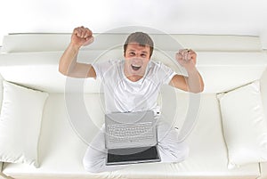 Happy young man sitting on the couch with arms up.