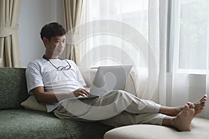 Happy young man sitting on couch in living room and using laptop computer