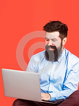 Happy young man sitting on the floor with and using laptop computer on red background. Holding laptop computer