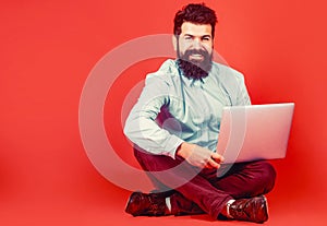 Happy young man sitting on the floor with and using laptop computer on red background. Holding laptop computer