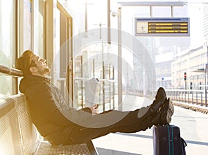 Happy young man sitting with travel bag at the train station