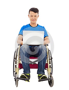 Happy young man sitting on a wheelchair with a laptop