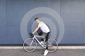 Happy young man sitting on a white bike against the wall, looking at the camera and smiling