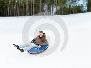 Happy young man sliding down on snow tube