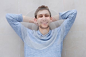Happy young man smiling with hands behind head by gray wall