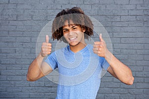 Happy young man smiling with thumbs up gesture against grey wall