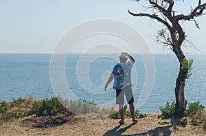 Happy young man standing on a cliff with his arms raised looks at the sea